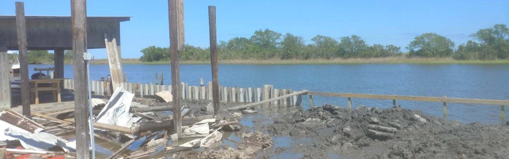Storm damaged boathouse, dock decking and timber bulkhead with debris and washed out ground along a Gulf Coast waterway